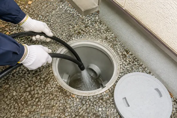 屋外の排水桝へ高圧洗浄のホースを入れる様子